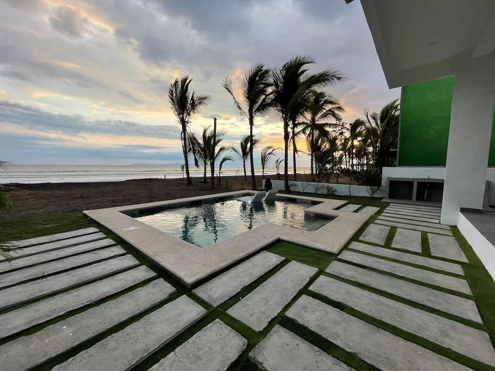 Piscina y palmeras en una casa de playa de Tivives mientras cae el sol sobre el Pacífico